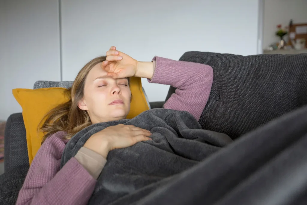 Kobieta odpoczywa na kanapie z ręką na czole - wieczorny wzrost temperatury
