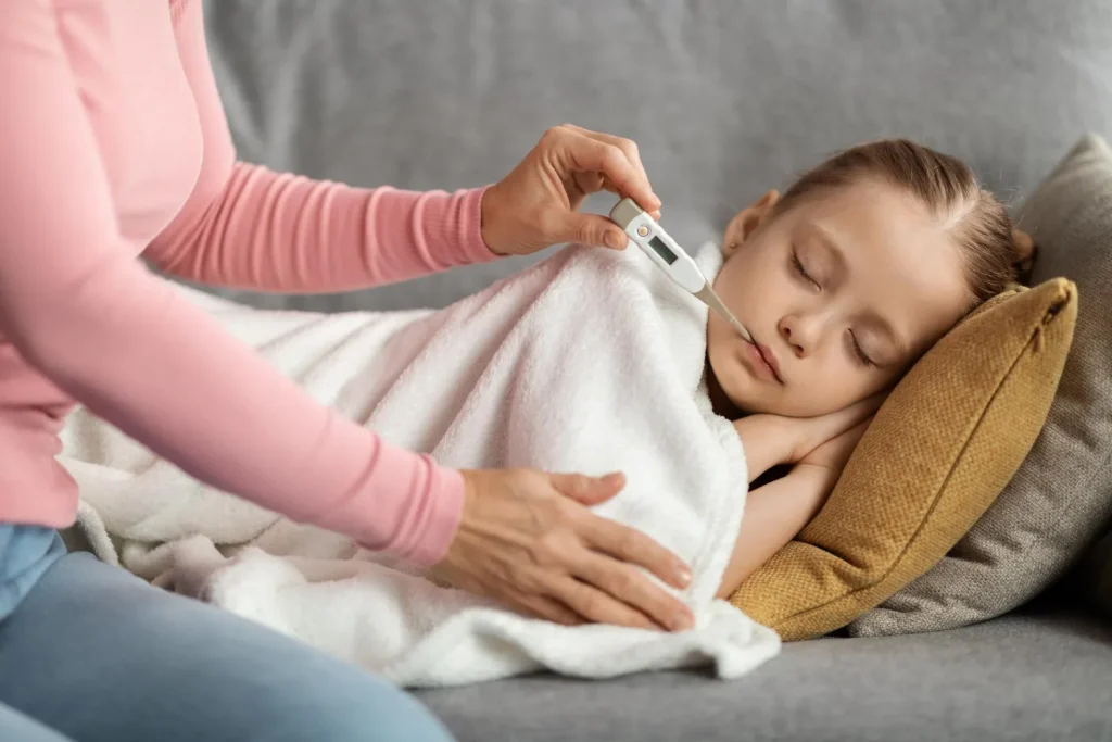 Mama mierzy temperaturę śpiącej córce - gorączka a pójście do szkoły